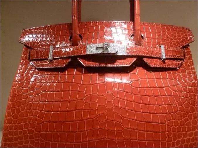 A Hermes Birkin in shiny orange crocodile with palladium hardware, showing the two top handles, flap and turnlock