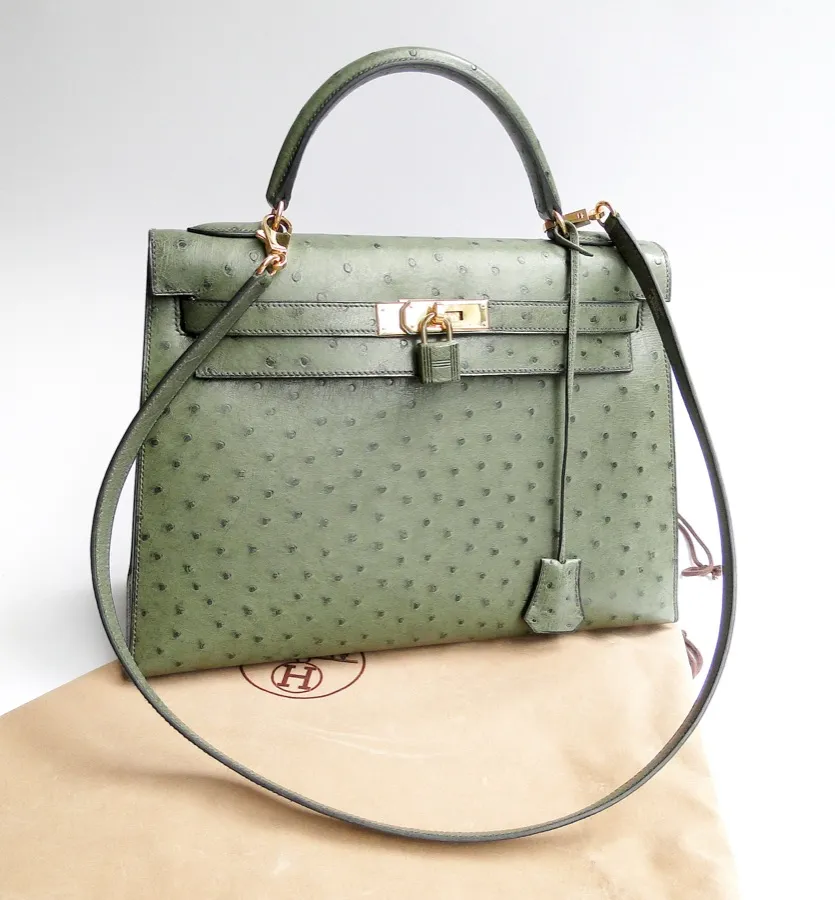 A Hermes Kelly in green ostrich leather with gold hardware, resting on its dust bag